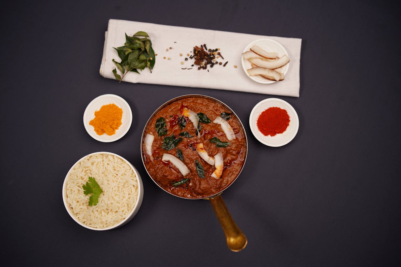 gallery-4 Top view of a traditional Indian curry served with rice and spices on a dark background.