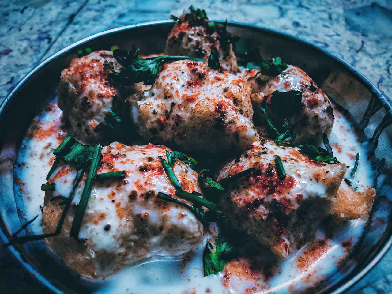 services-01 Close-up of traditional Indian dahi vada garnished with yogurt, herbs, and spices.