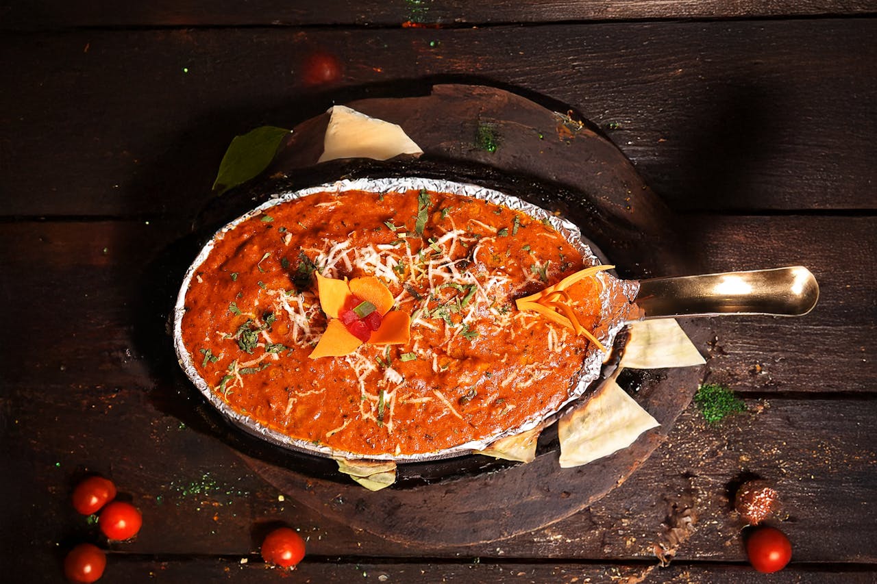 gallery-5 A flavorful Indian curry with vibrant garnish served in a metal dish, perfect for food lovers.