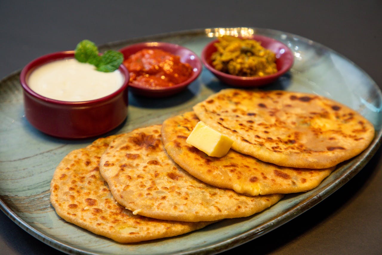 hero-img-02 Appetizing Indian paratha served with yogurt and pickles on a blue plate.