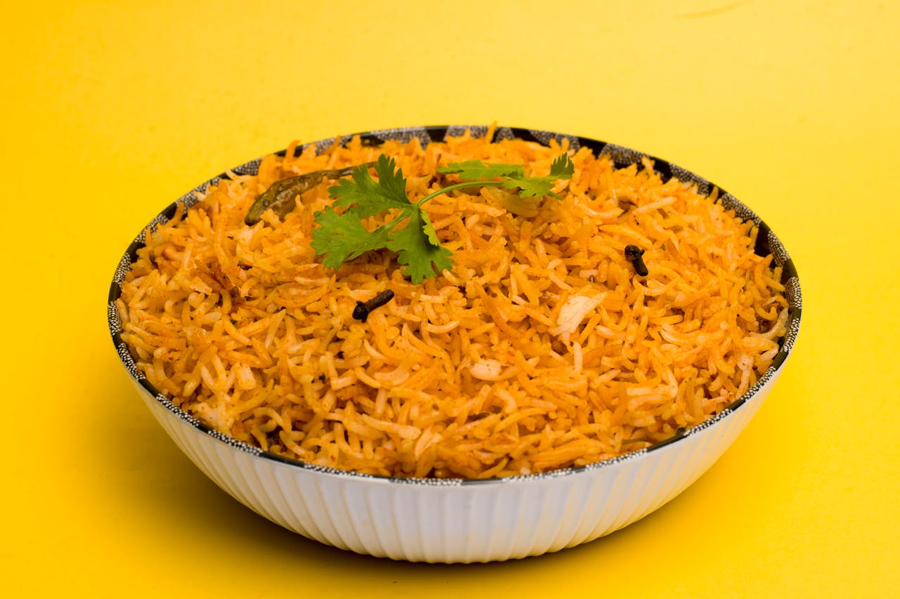 gallery-6 Aromatic Indian biriyani with spices served in a white bowl with a vibrant yellow background.