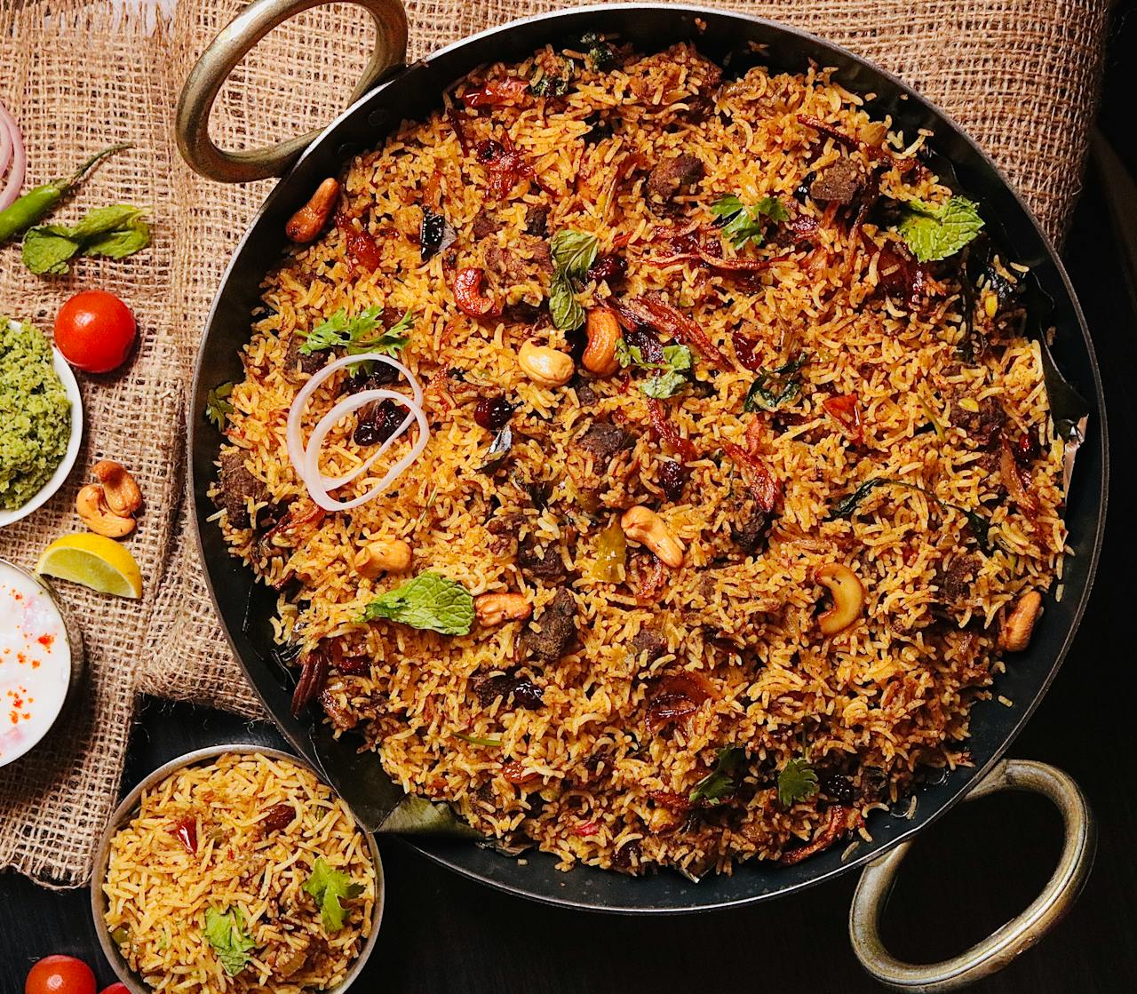 services-03 Top view of flavorful Indian biryani in a cooking pan, garnished with cashews and herbs.